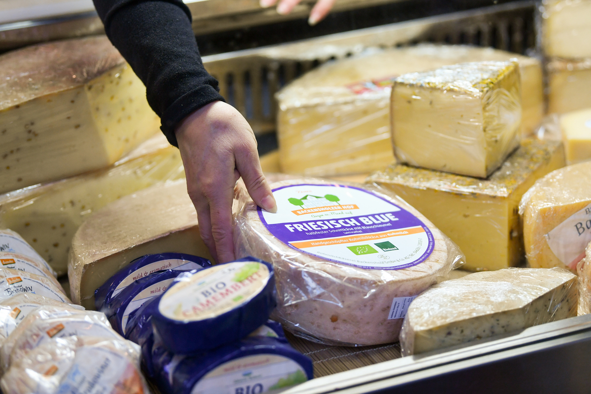 A saleswoman reaches for a cheese wheel.